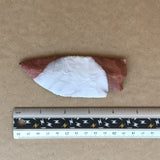 Reverse side, novaculite stone knife blade with red and white coloration next to a ruler on a brown background