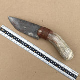 Flint bladed knife with antler handle next to a ruler on a brown background