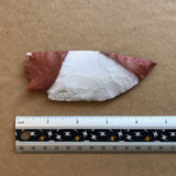Novaculite stone knife blade with red and white coloration next to a ruler on a brown background