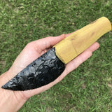 Hand holding a black obsidian blade with an Osage orange handle kit components against a grassy background