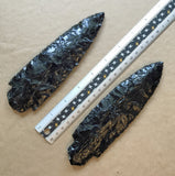 Two black obsidian blades with a ruler for scale on a brown background