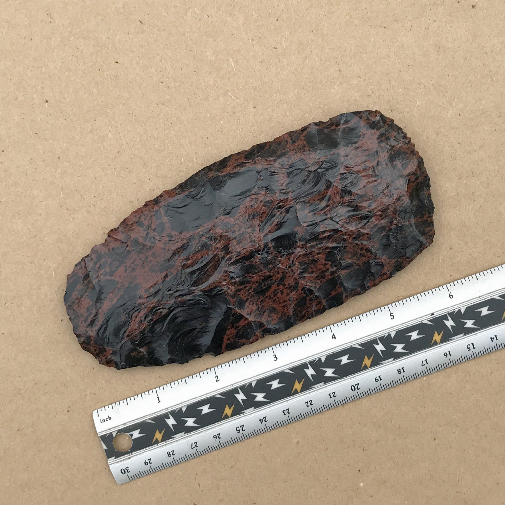Large mahogany axe blade next to a ruler on a brown background