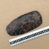 Large mahogany axe blade next to a ruler on a brown background