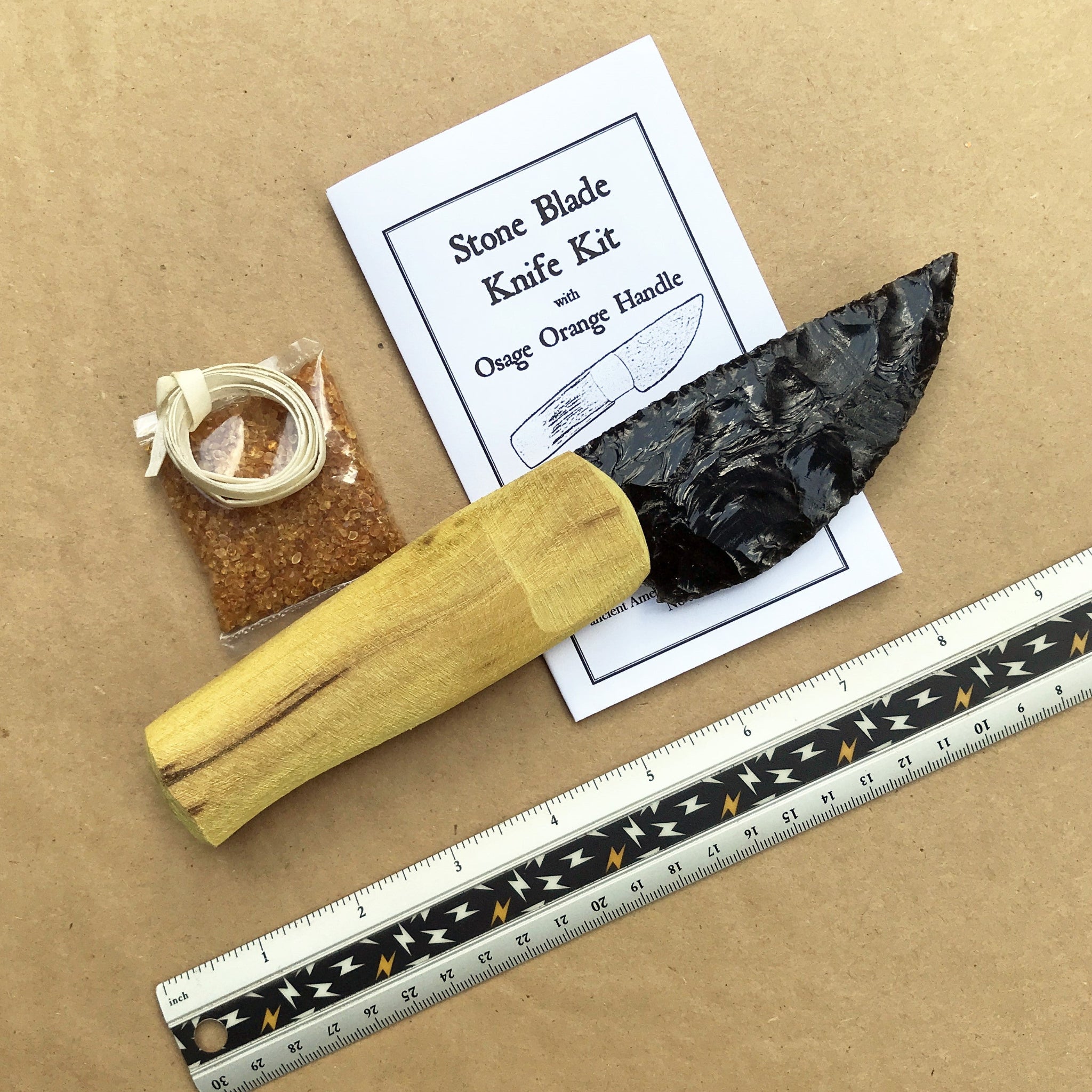 Black obsidian blade knife kit with Osage orange handle on a brown background, accompanied by a ruler for scale.