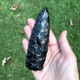 Black obsidian knapped blade with deep flaking in hand 
