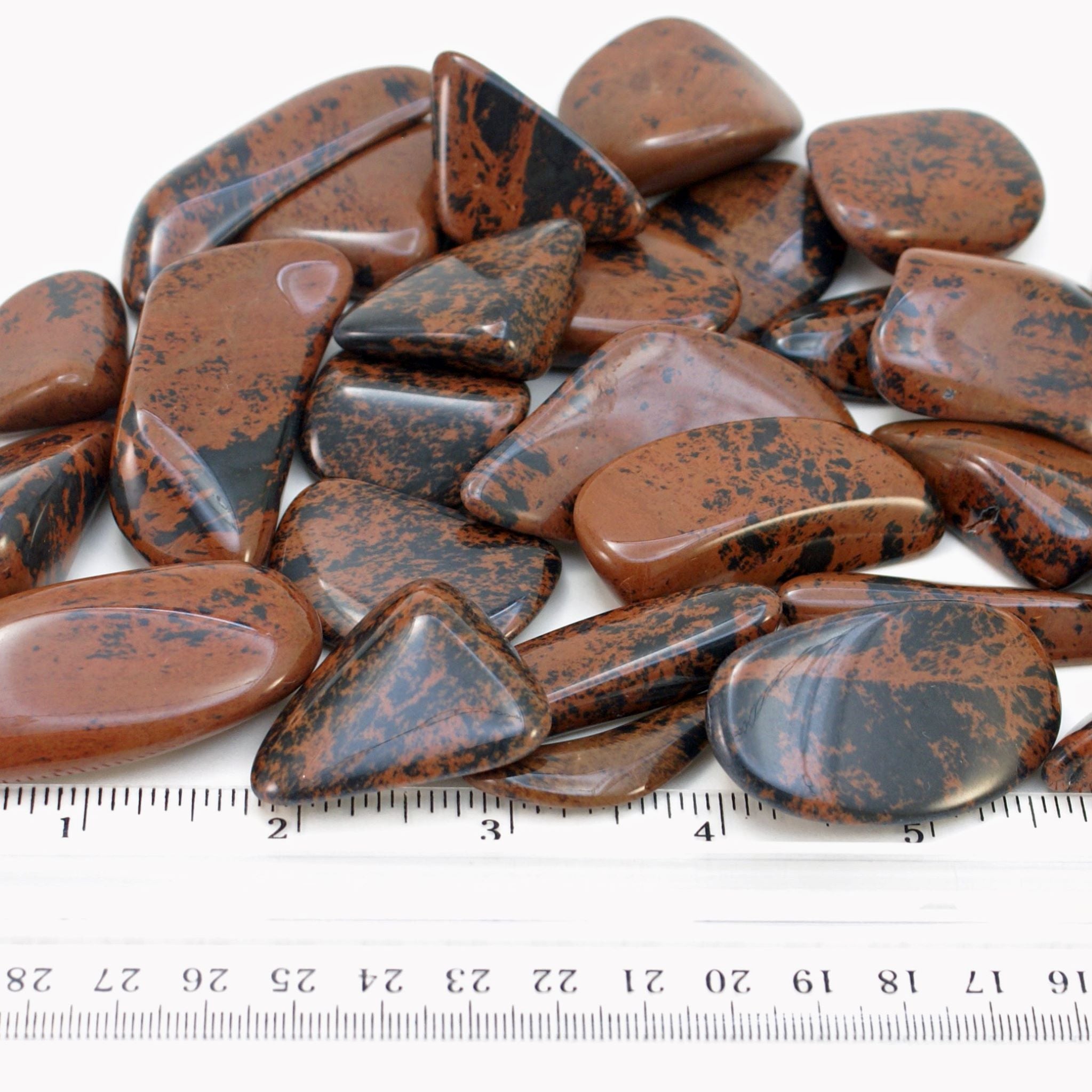 Close-up of tumbled mahogany obsidian stones with ruler